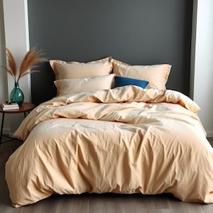May include: A beige duvet cover with a smooth, textured surface. The duvet cover is on a bed with two beige pillowcases and a blue pillow.