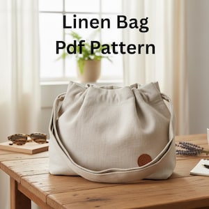 May include: A beige linen bag with a drawstring closure and a long shoulder strap sits on a wooden table. The bag has a small, round, brown leather patch. The text "Linen Bag Pdf Pattern" is displayed in black letters.