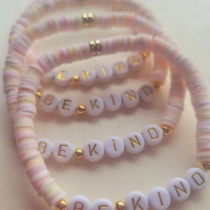 May include: Four pink and white beaded bracelets with gold beads and the words "Be Kind" spelled out on each bracelet.