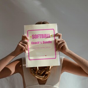 May include: A rectangular document titled Softball Coach's Bundle with a pink border and text. The document lists Lineups, Positions, Game Notes, and Practice Plans. It is held up, obscuring the face, and features a small red bow icon at the bottom.