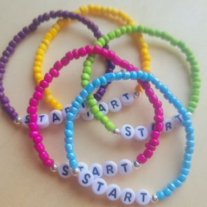 May include: Five colorful beaded bracelets with the word "START" spelled out in white letters on each bracelet.