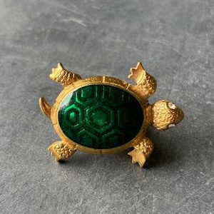 May include: A gold-tone turtle brooch with a green enamel shell and clear rhinestones for eyes.