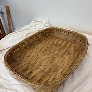 May include: A rectangular woven basket with a light brown finish, featuring a flat base and vertical sides constructed from interlaced strips. The basket has a consistent grid-like pattern throughout the bottom and walls, with a reinforced rim.