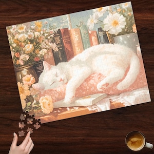 May include: A white cat sleeps on a pink and white floral pillow with a stack of books and flowers in the background.