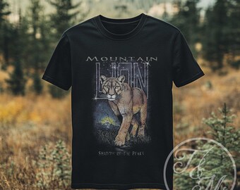 Könnte beinhalten: Schwarzes T-Shirt mit einem Berglöwen-Design. Der Text "MOUNTAIN LION" befindet sich über dem Bild und "SHADOW OF THE PEAKS" darunter. Die Grafik zeigt einen Berglöwen in einer natürlichen Umgebung mit Bergkulisse.