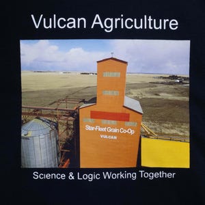 May include: Black t-shirt featuring a landscape image of an orange grain elevator with the text "Vulcan Agriculture" and "Star-Fleet Grain Co-Op". The phrase "Science & Logic Working Together" is also displayed.