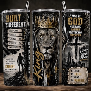 May include: A cylindrical tumbler with a metal straw featuring a lion wearing a gold crown, a silhouette of a person, a cross, and a city skyline. Text includes BUILT DIFFERENT, A MAN OF GOD, HUSBAND, FATHER, PROTECTOR, PROVIDER, and Bible verses.