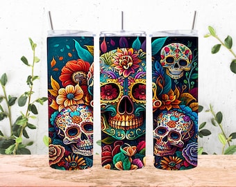 May include: Three colourful stainless steel tumblers with a Day of the Dead theme. Each tumbler features a sugar skull with floral designs and intricate details. The skulls are surrounded by vibrant flowers and leaves.