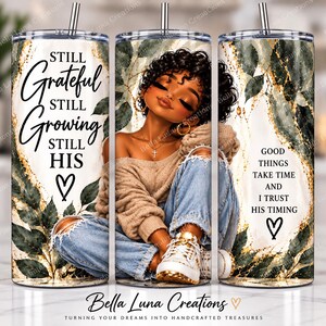 Può includere: Un bicchiere cilindrico con cannuccia in metallo che presenta la grafica di una persona con capelli ricci, maglione beige e jeans blu. Il design include foglie verde scuro, accenti dorati e il testo Still Grateful Still Growing Still His e Good Things Take Time And I Trust His Timing con simboli a cuore.