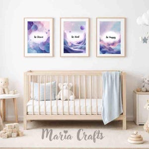 Puede incluir: Tres impresiones artísticas enmarcadas con las frases "sé valiente", "sé amable" y "sé feliz". La obra de arte presenta un diseño de acuarela en tonos morados, azules y rosas. Las impresiones se exhiben sobre una cuna de madera en un entorno de guardería.