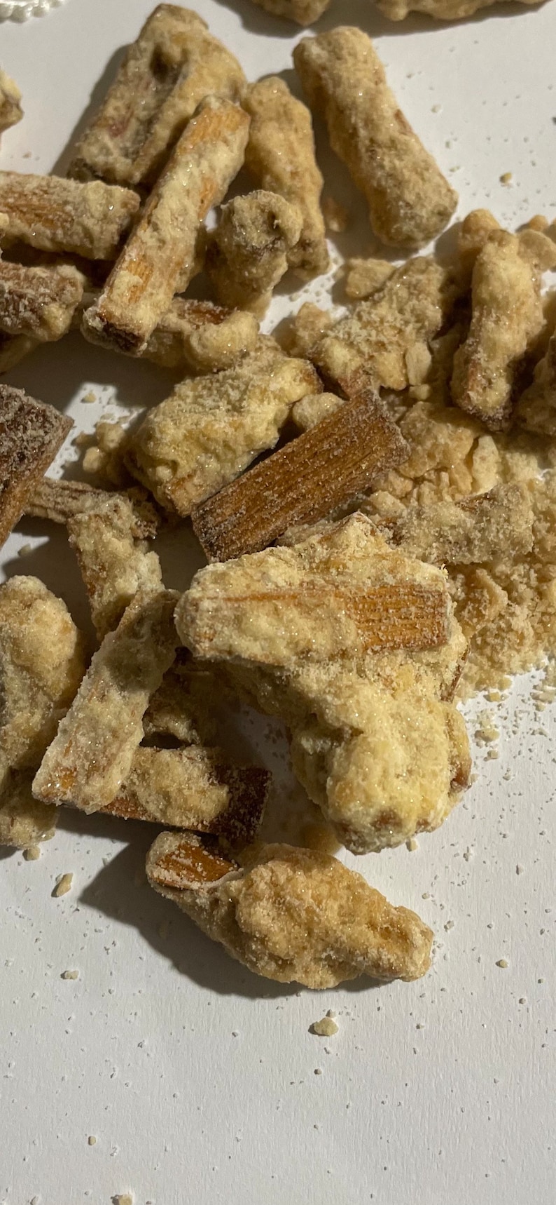 May include: A close-up of a pile of crispy, sugar-coated fried snacks. The snacks are light brown in color and have a grainy texture.
