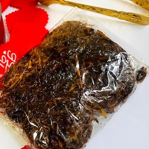 May include: A clear plastic bag filled with dark brown dried herbs. The bag is sitting on a white surface with red heart-shaped decorations that say "Be You" and "Love you".