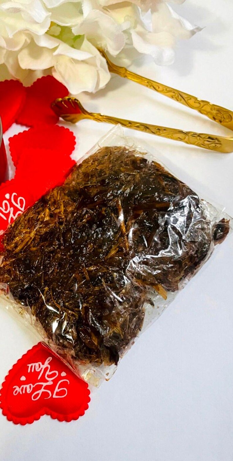 May include: A clear plastic bag filled with dark brown dried herbs. The bag is sitting on a white surface with red heart-shaped decorations that say "Be You" and "Love you".