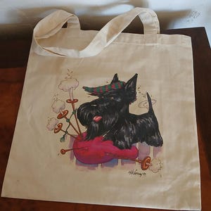 Puede incluir: Una bolsa de mano de lona beige con una ilustraci&oacute;n de dibujos animados de un terrier escoc&eacute;s negro tocando la gaita. El perro lleva un sombrero a cuadros verde y rojo. La bolsa tiene dos asas y forma rectangular. El dise&ntilde;o incluye una gaita roja y humo blanco.