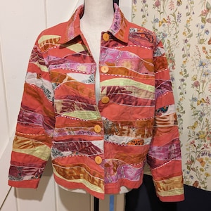 Könnte beinhalten: Eine rote, rosa und orangefarbene Patchworkjacke mit Knopfleiste und langen Ärmeln. Die Jacke besteht aus verschiedenen Stoffen und hat einen einzigartigen, bohemischen Stil.