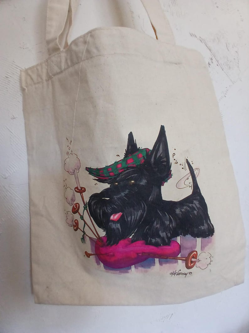 Puede incluir: Bolso tote de lona beige con un Terrier escoc&eacute;s negro con un sombrero a cuadros verde y rojo, tocando una gaita rosa. El perro tiene la lengua fuera. El bolso tiene un asa.