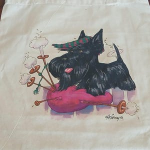 Puede incluir: Bolso tote de color crema con una ilustraci&oacute;n de dibujos animados de un Scottish Terrier negro tocando la gaita. El perro lleva un sombrero a cuadros y descansa sobre una gaita rosa. La gaita tiene detalles en marr&oacute;n y dorado. La firma del artista es visible.