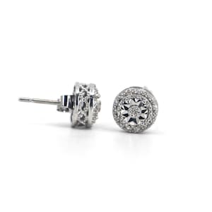 May include: A pair of silver stud earrings with a round, pave-set diamond center and a delicate, filigree design around the edge.