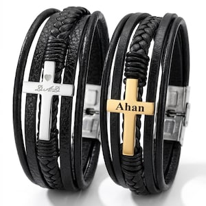 May include: Two black leather bracelets with silver and gold cross pendants. One cross has the inscription "De&D" and a heart, the other reads "Ahan". The bracelets have multiple leather strands and braided accents.