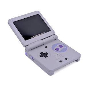 May include: A light gray Game Boy Advance SP handheld game console. The console features a black screen, a directional pad, and purple buttons. The text "GAME BOY ADVANCE SP" is visible on the screen.