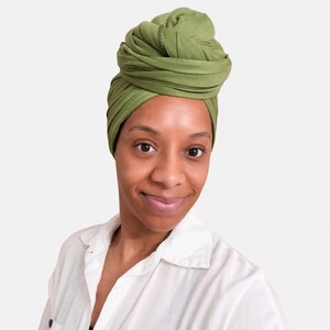 May include: A woman wearing a green turban and a white button-down shirt. The turban is a vibrant shade of green, and the shirt is crisp and clean. The woman is smiling, and the background is a plain white.