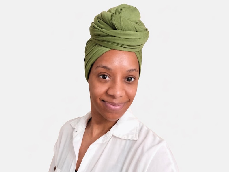 May include: A woman wearing a green turban and a white button-down shirt. The turban is a vibrant shade of green, and the shirt is crisp and clean. The woman is smiling, and the background is a plain white.