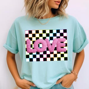 May include: A light blue t-shirt with a checkered pattern and the word "LOVE" in pink fuzzy letters.