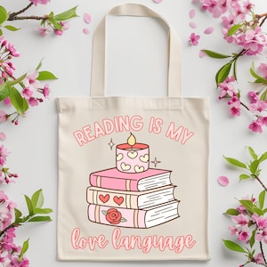 Op de afbeelding: Een witte tote bag met een roze en wit ontwerp. De tas heeft een stapel boeken met een brandende kaars erop. De tekst op de tas is "Reading is my love language".