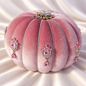 May include: A round, pumpkin-shaped clutch bag crafted from soft, dusty pink velvet. The exterior features vertical rows of clear rhinestones, decorative pink crystal brooches with dangling teardrop stones, and a central floral crystal clasp.