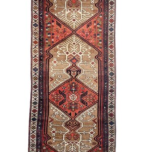 May include: A traditional runner rug with a geometric pattern in shades of red, brown, and white. The rug has a fringe border and is rolled up.