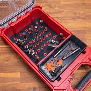 Peut inclure: Une boîte à outils rouge avec un couvercle transparent, ouverte pour révéler un assortiment d'outils. L'intérieur comprend un insert noir avec divers forets et un compartiment séparé avec des clés et d'autres outils. La boîte à outils est sur une surface en bois.