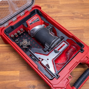 Könnte beinhalten: Ein roter Werkzeugkoffer mit transparentem Deckel, der einen Router und verschiedene Bits enthält. Der Koffer ist geöffnet und zeigt die Werkzeuge im Inneren. Der Router ist rot und schwarz, und die Bits sind ordentlich angeordnet. Der Koffer hat einen Griff.