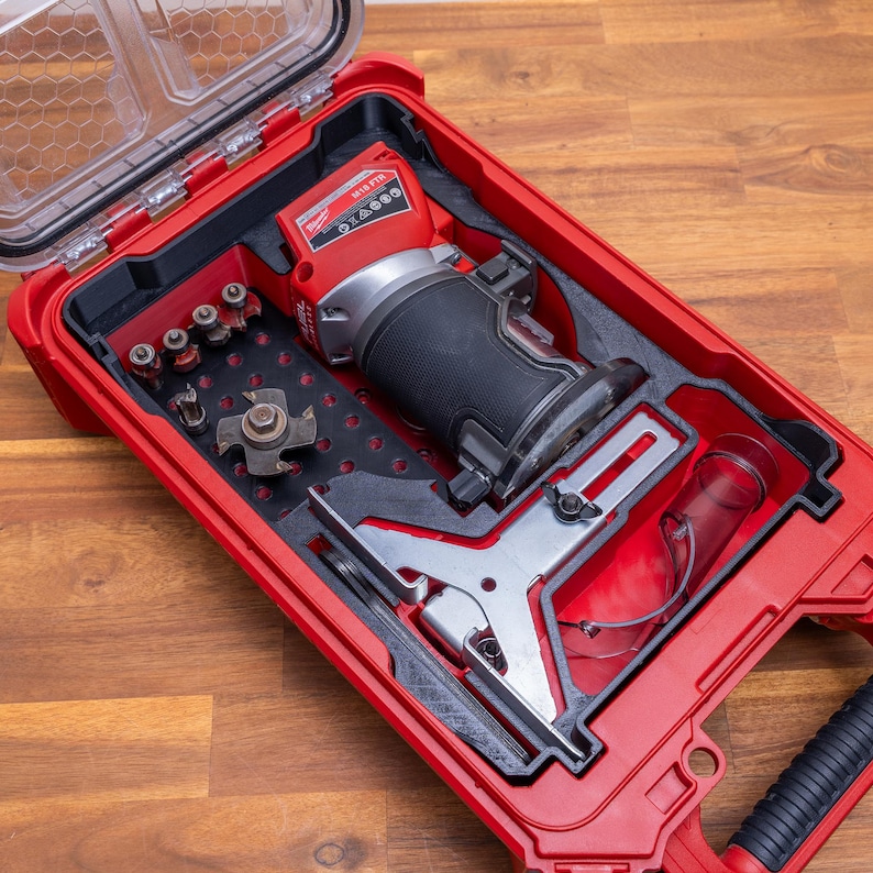 May include: A red Milwaukee M18 FTR cordless compact router stored in a matching red hard plastic carrying case. The case includes custom foam inserts holding the router, a metal edge guide, a clear dust shroud, and several router bits.
