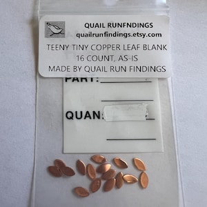 May include: A clear plastic bag containing small copper leaf blanks. The label reads "QUAIL RUNFNDINGS" and "TEENY TINY COPPER LEAF BLANK 16 COUNT, AS-IS". The copper leaves are oval-shaped and have a metallic finish.
