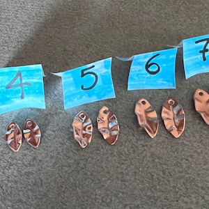 May include: Seven pairs of small, rose gold-colored metal leaf charms. Each pair is numbered 4 through 7 on blue sticky notes.