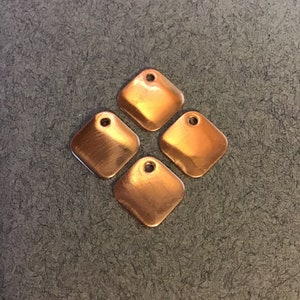 May include: Four copper-colored metal diamond-shaped charms with a hole at the top for attaching to a necklace or bracelet.