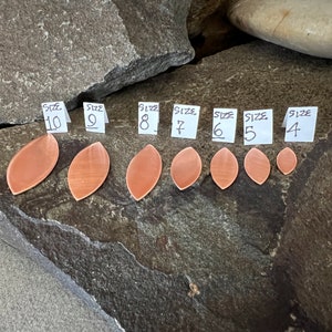 May include: A set of eight copper leaf-shaped pendants in various sizes, labeled with numbers 4 through 10. The pendants are arranged in a row on a gray and brown rock surface.