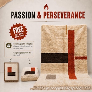 May include: A large, cream-colored, shaggy rug with a geometric pattern of dark brown and rust-orange stripes and a small gray rectangle. The rug features a fringed bottom edge. A matching framed rug and a square wool pouf are displayed nearby.