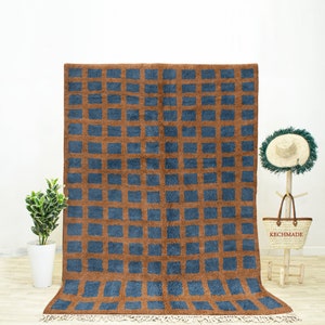 May include: A brown and blue geometric patterned rug with a fringe border. The rug has a checkered pattern with blue squares on a brown background.