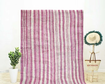 May include: A pink and white striped rug with a fringe border. The rug is made of wool and is hand-woven. It is a traditional Moroccan rug.