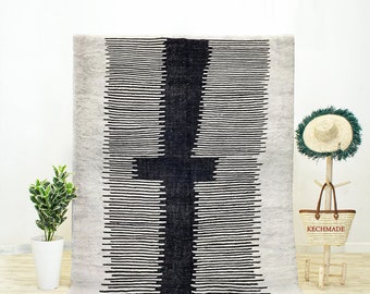 May include: A black and white striped rug with a large black geometric design in the center. The rug has a fringe border and is on a white background.