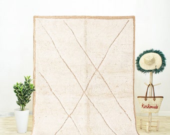May include: A white Moroccan rug with a diamond pattern woven into the fabric. The rug has a fringe border and is made of wool.