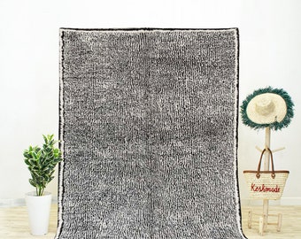 May include: A black and white Moroccan rug with a textured, woven design. The rug has a fringe border.