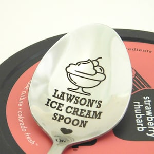 May include: A silver spoon with a black engraved design of an ice cream sundae and the text "Lawson's Ice Cream Spoon".