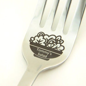 May include: A silver fork with a black and white design of a bowl of salad with the text "Tommy's Salad" engraved on the handle.