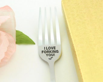 May include: A stainless steel fork with the words "I LOVE FORKING YOU!" etched on the handle. The fork has four prongs and a heart symbol. A gold-coloured gift box is in the background.