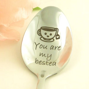 May include: A silver spoon with the text "You are my bestea" engraved on it. A cartoon teacup with a smiley face is above the text.