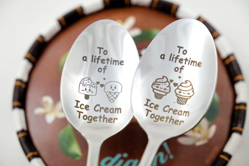 Puede incluir: Dos cucharas de plata con conos de helado y paletas de helado grabados. Las cucharas tienen el texto "To a lifetime of Ice Cream Together".