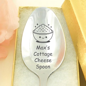 May include: A stainless steel spoon with the text "Max's Cottage Cheese Spoon" engraved on the handle. The spoon features a cartoon illustration of a bowl of cottage cheese. The spoon is in a gold gift box.