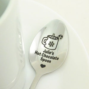 May include: A silver spoon with a black engraved design of a mug of hot chocolate with marshmallows and a candy cane. The text "Julie's Hot Chocolate Spoon" is engraved below the mug.